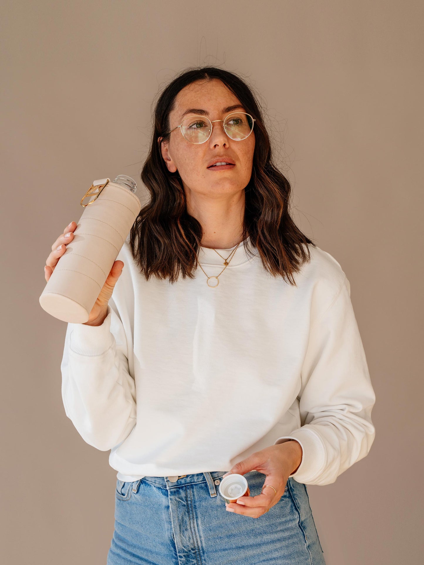 Girl drinking from glass bottle with beige faux leather cover