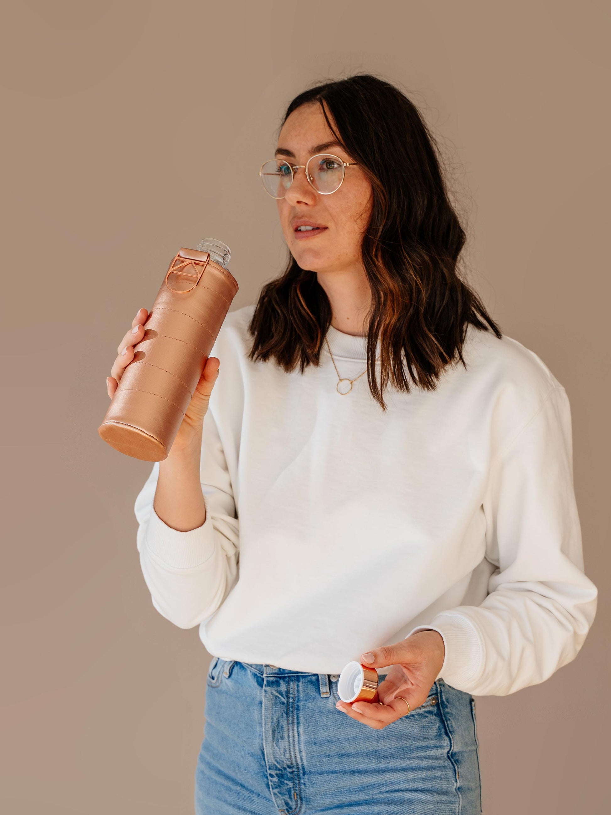 Girl drinking from glass bottle with bronze faux leather cover