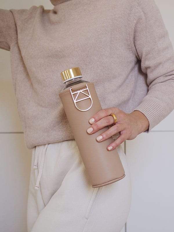 Glass water bottle with gold details and beige faux leather cover by EQUA